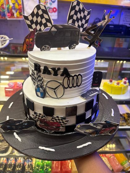 A two-tier race car theme cake with checkered flags and logos of Audi, BMW, and Mercedes. This cake is a speed lover's dream, perfect for celebrating a milestone with a touch of luxury and excitement.