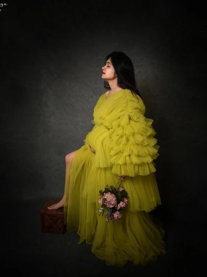 A full-body profile shot that showcases the dramatic silhouette of this tiered tulle gown, creating a high-fashion maternity look.