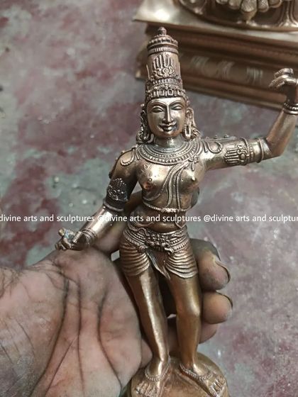 A small, finely detailed bronze sculpture of Lord Rama in the process of being finished. The artisan's hand gives a sense of the delicate work involved in creating even small icons.
