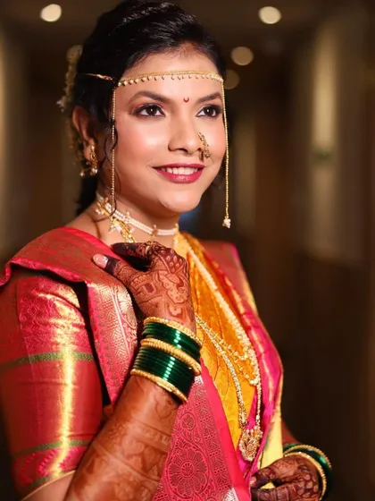 A classic Maharashtrian bridal look. The bride is wearing a traditional yellow and pink saree, with her makeup kept soft and glowing to highlight her natural beauty.