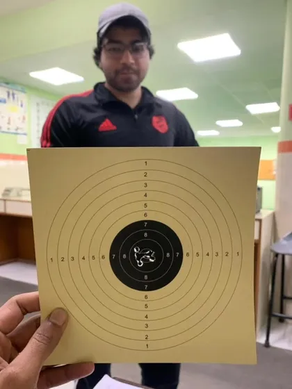 A student holding up his target, showing a very tight grouping of shots in the center. This is the result of consistent practice.