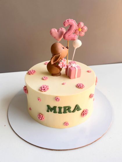 A dreamy cake for Mira's second birthday, featuring soft pastels, tiny florals, and a cute, hand-sculpted bunny topper holding a gift and balloons.