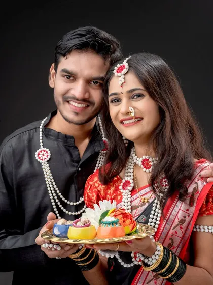 A happy couple celebrating Makar Sankranti in the studio. They are dressed in matching black outfits and halwyache dagine, holding a platter of treats.