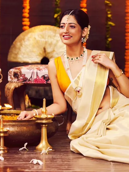A jewellery campaign with a traditional South Indian theme. The warm lighting from the diyas creates a beautiful, festive glow, highlighting the intricate gold jewellery and the classic Kasavu saree.