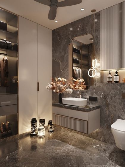 We kept the base neutral yet added a blingy twist to this bathroom design. The dark grey marble provides a moody backdrop for the modern vanity, halo-lit mirror, and an integrated walk-in closet section with glass doors and internal lighting.