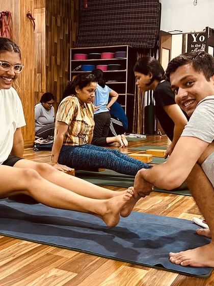 Partner work is key to learning. Here, students assist each other in an arm-strengthening pose using blocks for support.