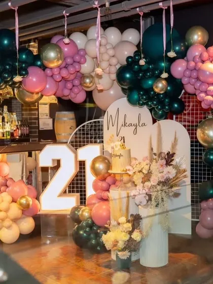 A stylish 21st birthday party with a moody and romantic theme. The decor features a rich color palette of deep greens and pinks, with organic balloon garlands creating a luxurious feel.
