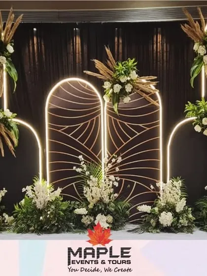 An elegant stage backdrop designed for a corporate awards ceremony. The design features modern arches with integrated neon lighting, complemented by lush white and green floral arrangements for a sophisticated and celebratory look.