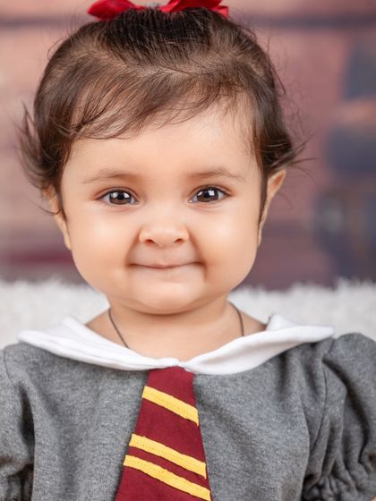 A sweet, smiling portrait of a baby girl dressed in her Hogwarts uniform. She's ready to bring some magic into the world.