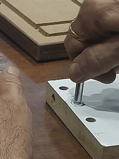 A trainer demonstrates how to insert a mini-fix connector into a pre-drilled hole on a piece of panel board, a core skill for modular furniture assembly.