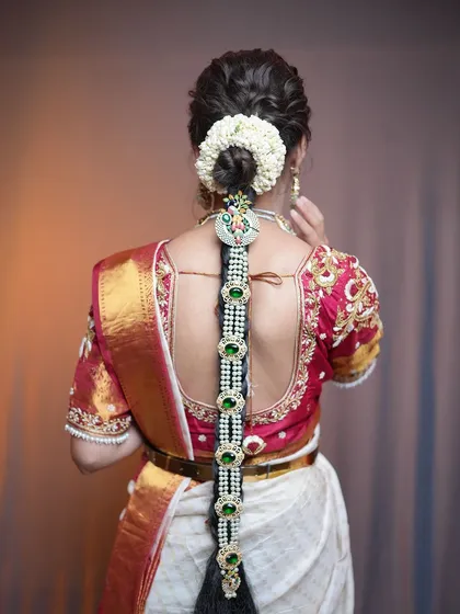 A traditional South Indian bridal braid, or jada, featuring jasmine flowers and stunning pearl and green stone jewelry. This is a classic hairstyle that I specialize in for wedding ceremonies.