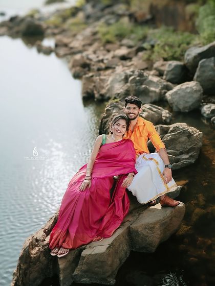 A beautiful portrait of the couple sitting on rocks by the river. The vibrant colors of their traditional outfits stand out against the natural backdrop.