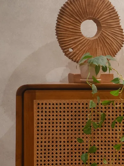 A detail of the 'Kayo' cabinet, showing the beautiful texture of the rattan door, complemented by a decorative wooden piece and a trailing plant.