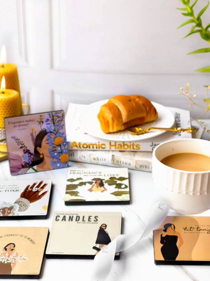 A cozy morning scene featuring illustrated cards, a cup of coffee, a croissant, and lit beeswax candles. The warm lighting and lifestyle elements make the products feel part of a beautiful daily ritual.