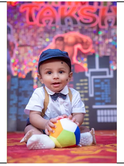 A sweet portrait of a baby boy looking directly at the camera, with a colorful city and superhero backdrop creating a fun theme.