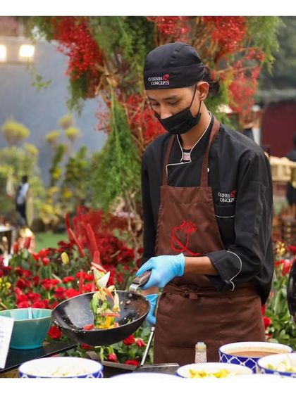 A chef tosses vegetables in a pan at a live station, set against a beautiful floral backdrop. This demonstrates our ability to create visually appealing cooking setups that enhance the event's overall aesthetic.