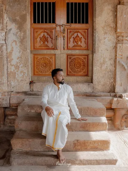 A groom-to-be sits thoughtfully on the stone steps of a temple, in front of an ornate wooden door, creating a timeless and masculine portrait.