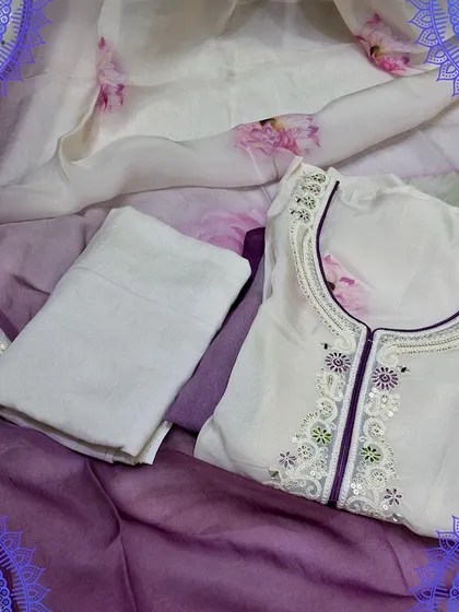 An elegant white and purple dress material set. The top has delicate embroidery, and the organza dupatta features a beautiful digital floral print, perfect for a graceful look.