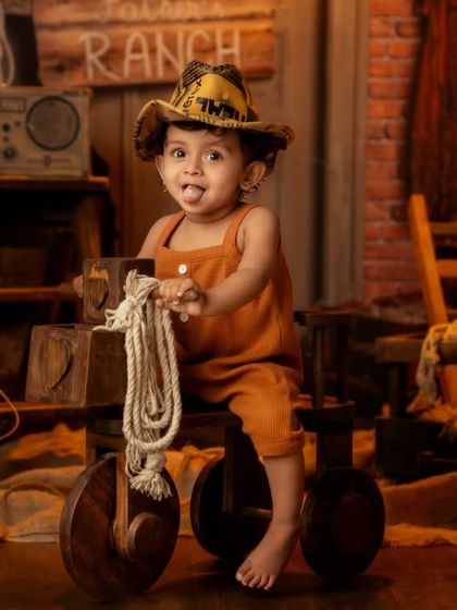 This little cowboy is having a blast, playing with a rope on his wooden tricycle in a fun, ranch-themed setting.