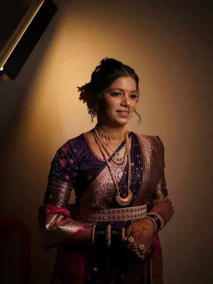 A full-length portrait of the bride in her purple Paithani. The makeup and hairstyle are designed to complement the richness of the saree.