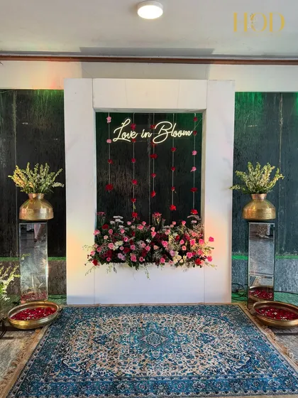 The full view of the "Love in Bloom" photo booth, complete with a traditional blue rug and brass urlis, blending modern and classic elements.