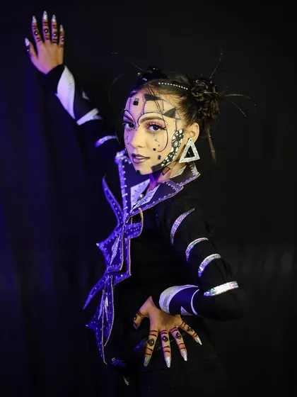 A full-body pose showcasing the complete geometric look, including the intricate nail and hand art that complements the facial makeup.