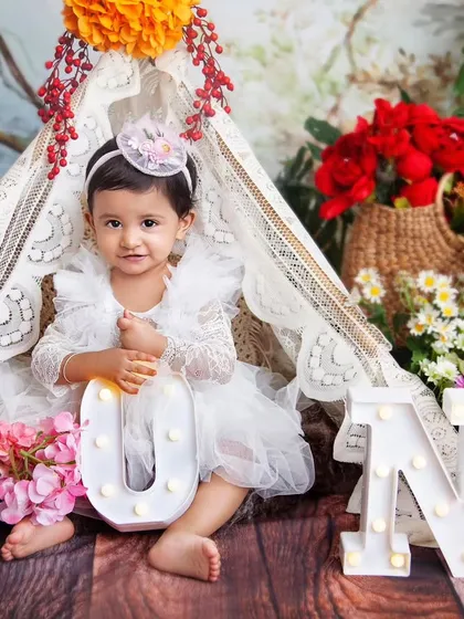 The joy of turning one! This little girl is sitting inside a beautiful lace teepee, surrounded by colourful flowers and holding light-up 'ONE' letters.