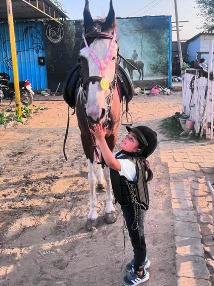 A young girl pets her horse, who is wearing a medal. It's a sweet moment of shared victory and affection.