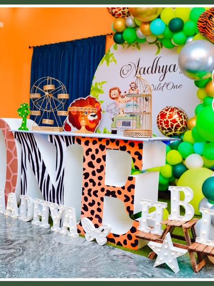 A "Wild One" jungle theme with large 'ONE' marquee letters. This setup features animal-print letters, character cutouts, and a green and gold balloon arch.