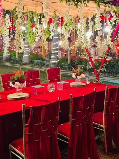 A bold and festive seating arrangement using a rich red color theme. The red velvet tablecloth and chair covers, paired with hanging floral installations, create a warm and celebratory mood perfect for holiday parties or themed corporate events.