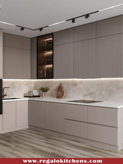 This L-shaped kitchen features textured, fluted upper cabinets in a dark wood finish, contrasted with smooth beige base cabinets. The track lighting and marble backsplash add to the modern, sophisticated feel of the space.