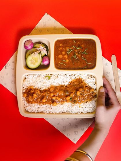 A top-down shot of a chole rice meal-box against a bold red background. This clean, graphic style is perfect for food delivery menus and apps.