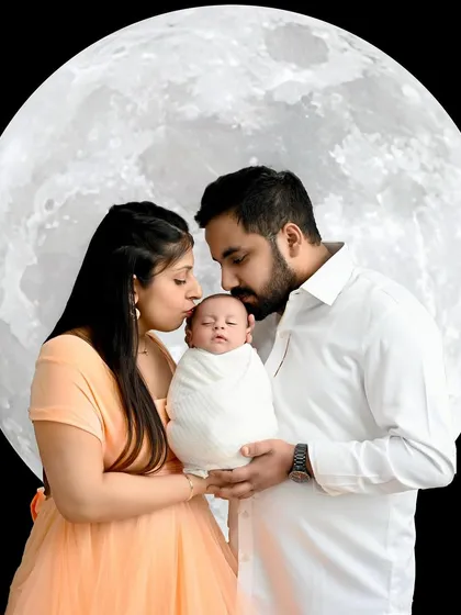 A dreamy "love you to the moon and back" portrait. This creative photo shows the parents kissing their newborn, silhouetted against a giant, glowing moon.