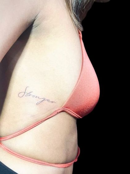 The final "Stronger" rib cage tattoo. The fine line script is elegant and subtle.
