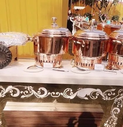 A section of our buffet table showcasing ornate copper chafing dishes and a unique seashell-shaped serving platter, highlighting our diverse range of premium equipment.