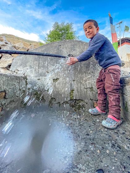A young boy in a Spiti village plays with water from a public tap. It's a simple, candid moment of daily life in a remote Himalayan community.