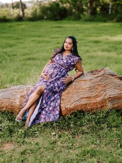 A wider perspective of the same peaceful outdoor setting. This shot captures more of the expansive green landscape, making the expecting mother look like she is one with nature.