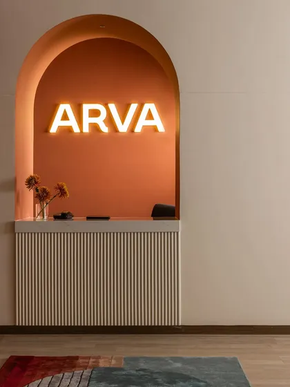 The arched reception desk at ARVA Clinic, a design element with a story. Inspired by the idea of a London phone booth turned inside out, it transforms a symbol of private calls into a welcoming space for open conversation, highlighted by the warm glow of the brand's name.