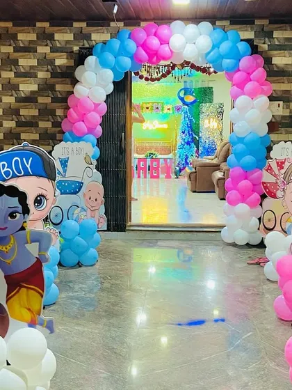 A baby shower entrance decorated with character cutouts and a pink, blue, and white balloon arch.