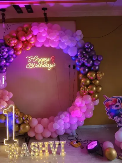 A unicorn-themed first birthday with a purple, pink, and gold balloon circle and a light-up name display.