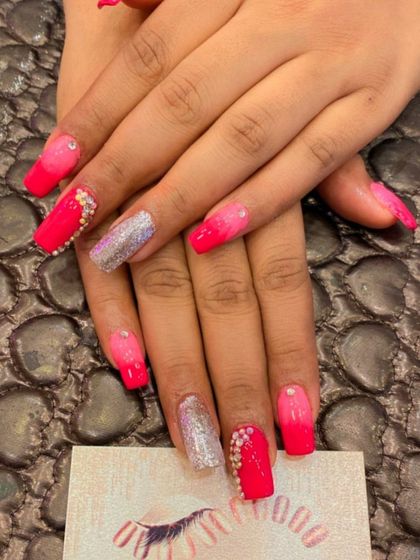 A vibrant set of hot pink and silver glitter nails. The design features a pink ombre effect and is heavily embellished with pearl-like crystals for a luxurious finish.