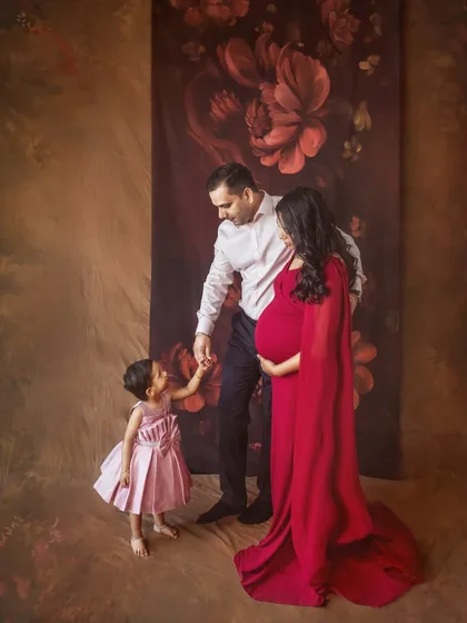 A heartwarming family moment as the parents-to-be interact with their young daughter. This shot beautifully captures the dynamic of a growing family in a classic studio setting.