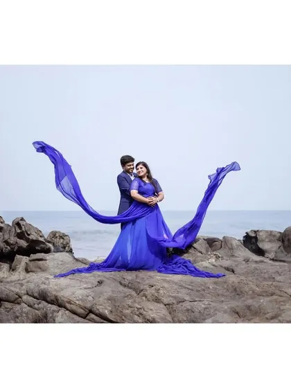 A dramatic "flying gown" shot on the rocks. The blue trail creates a beautiful wing-like shape against the sky, perfect for a statement pre-wedding photo.
