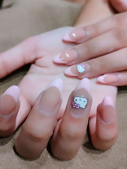 A cute and trendy manicure featuring a Hello Kitty charm on a sheer, almond-shaped nail extension.