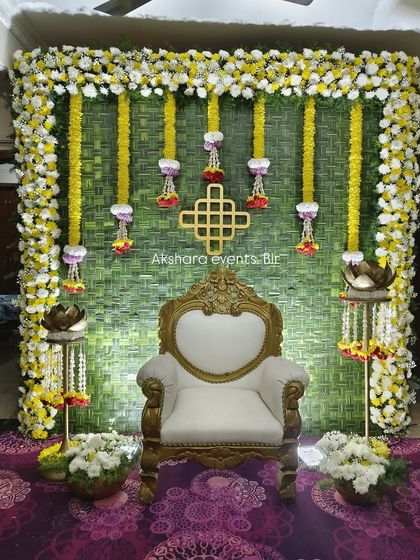 A traditional backdrop made from woven green leaves, decorated with yellow marigold garlands and lotus hangings. The ornate white and gold chair completes this classic Seemantham setup.