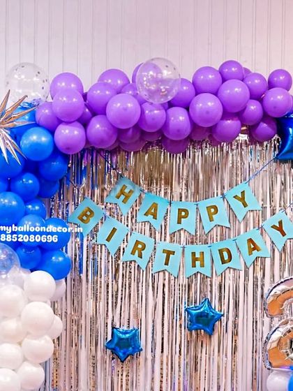 A birthday backdrop with a silver fringe curtain and a balloon garland in shades of purple, blue, and white. The number '2' foil balloon makes it perfect for a second birthday party.
