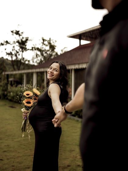 A beautiful "follow me" shot with the mom-to-be leading her partner towards a lovely country house, a bouquet of sunflowers in her hand.
