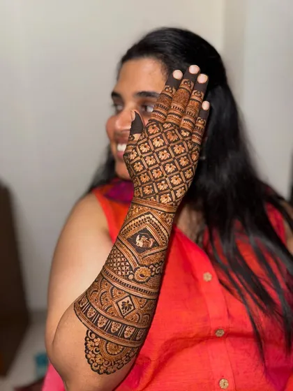 A happy bride showcasing her stunning back-of-hand mehendi. The design features a classic grid pattern, which is a timeless and elegant choice.