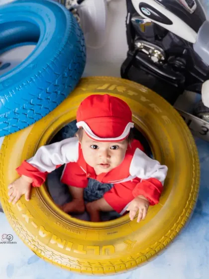 A few action shots from an F1 and racing-inspired photoshoot. The baby is styled in a red racing uniform, captured with fun expressions among tires and toy vehicles.