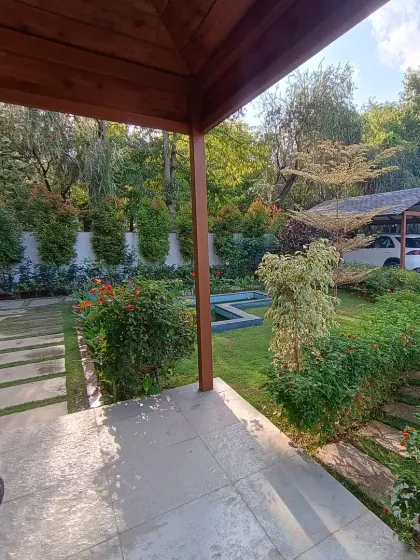 A balanced composition of hardscaping and softscaping, with a stone path leading through the garden towards a covered car park, surrounded by dense greenery.